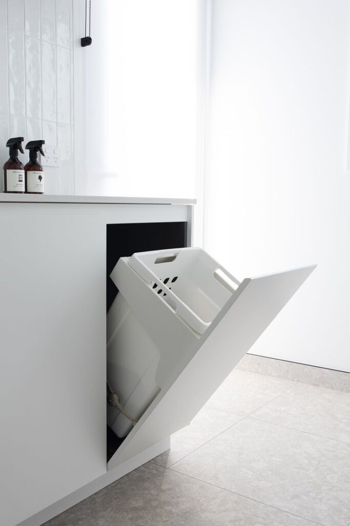White pull-out laundry hamper integrated into custom cabinetry for hidden storage