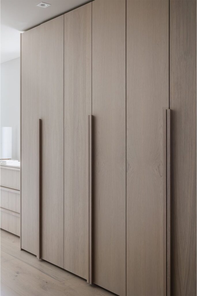 Floor-to-ceiling woodgrain wardrobe doors with long matching timber handles for a seamless look