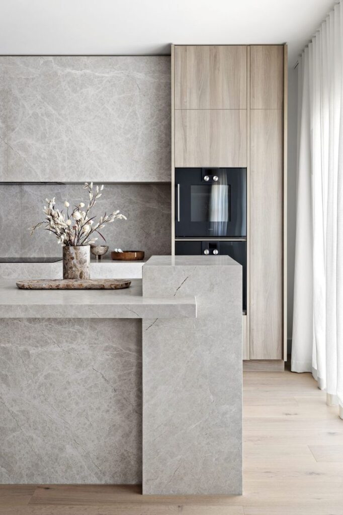 Grey island with a marble-pattern finish and matching splashback for a cohesive kitchen design